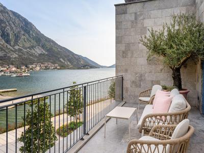 Balkon mit Korbstühlen und Kissen mit Blick auf das Meer und Berge bei klarem Himmel.