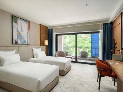 Chambre d'hôtel moderne avec deux lits simples, bureau et balcon avec vue sur la verdure.