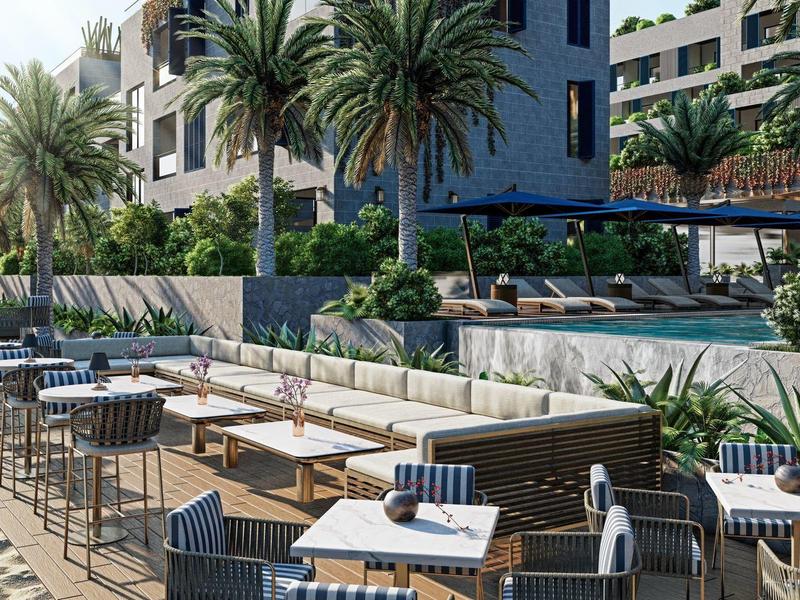 Strandrestaurant mit Tischen, Sesseln und Palmen vor einem Hotel mit Pool.