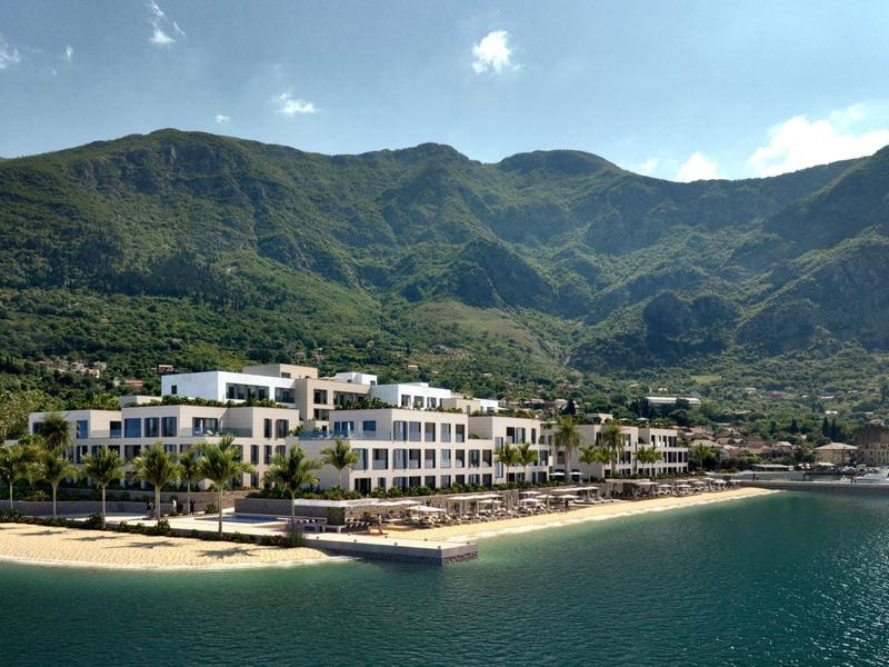 Hotelgebäude am Ufer mit Bergen im Hintergrund und klarem Himmel.