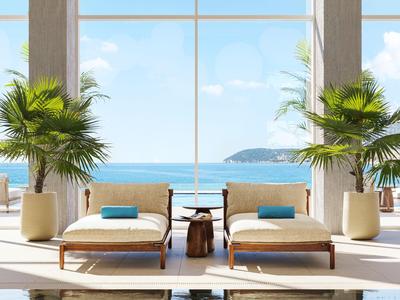 Deux chaises longues avec coussins à côté d'une piscine donnant sur la mer et le ciel à travers de grandes fenêtres.