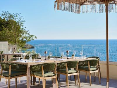 Terrasse mit gedecktem Tisch und Stühlen mit Blick auf das blaue Meer unter blauem Himmel.