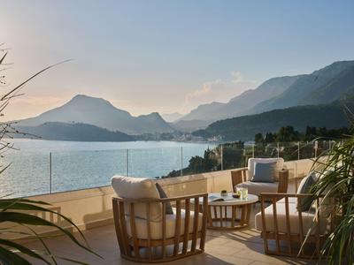 Terrasse mit Sitzmöbeln und Blick auf Berge und Wasser bei Sonnenuntergang.