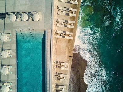 Top-down Ansicht eines Pools neben einer Strandpromenade mit Wellen am Ufer.