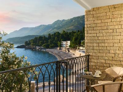 Balkon mit Tisch und Stühlen, Blick auf Strand, Meer und Berge bei Sonnenuntergang.