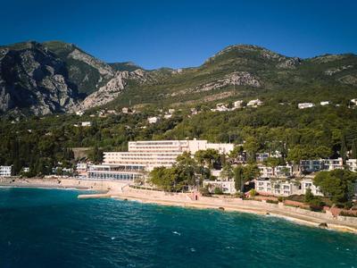 Kompleks hotelowy przy piaszczystej plaży z widokiem na zalesione góry i turkusowe morze.