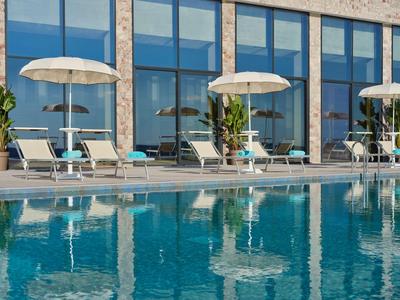 Moderner Poolbereich mit Liegestühlen, Sonnenschirmen und Glasfassade im Hotel.