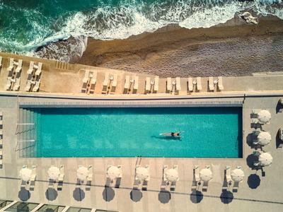 Vogelperspektive eines rechteckigen Pools mit Sonnenliegen an einem Strandhotel.