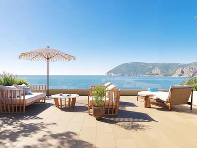 Terrasse mit Sitzmöbeln und Sonnenschirm mit Blick auf das Meer und die Küste bei klarem Himmel.