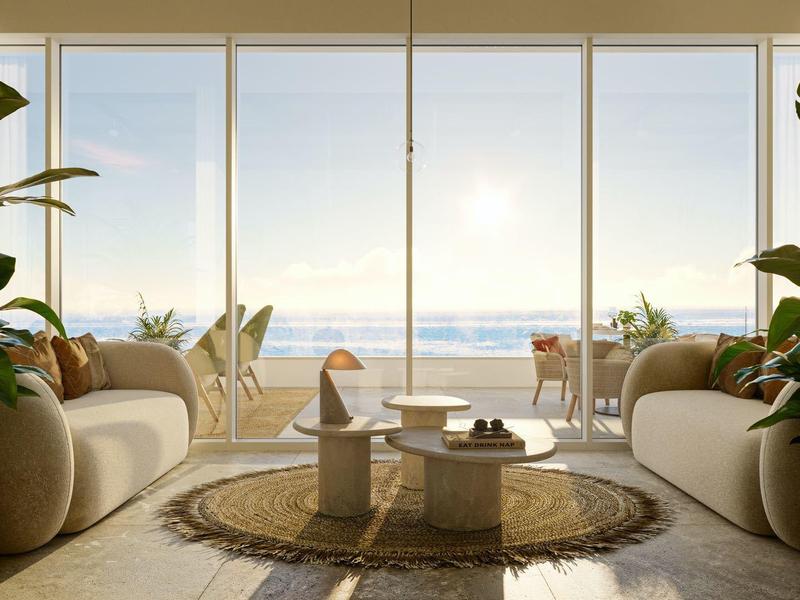 Helle Lounge mit zwei Sofas, Pflanzen und Blick auf das Meer durch große Fenster.