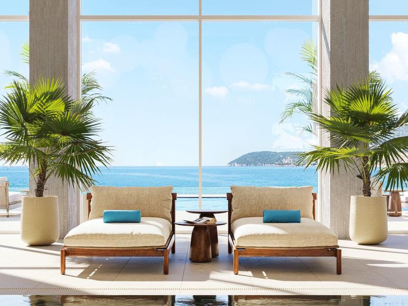 Moderne Lounge mit zwei Liegestühlen, Palmen und Meerblick durch große Fenster.