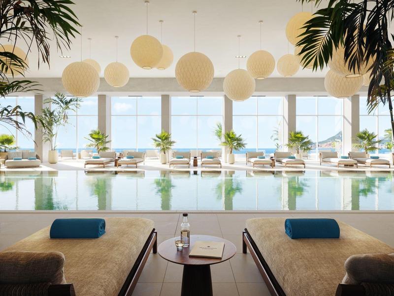 Moderner Indoor-Pool mit Liegen, Palmen und großen Fenstern mit Blick nach draußen.