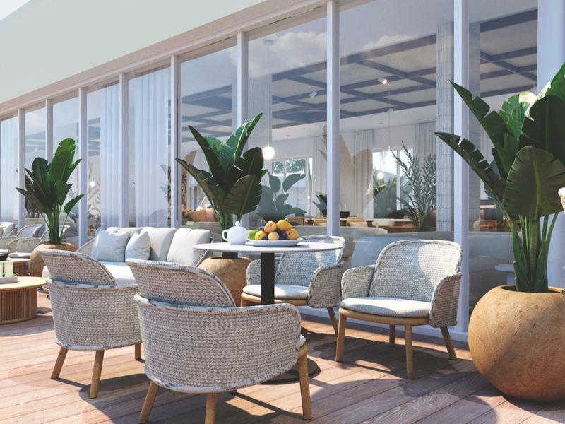 Terrasse eines Hotels mit Sitzbereichen und großen Blumentöpfen unter Glasfenstern.