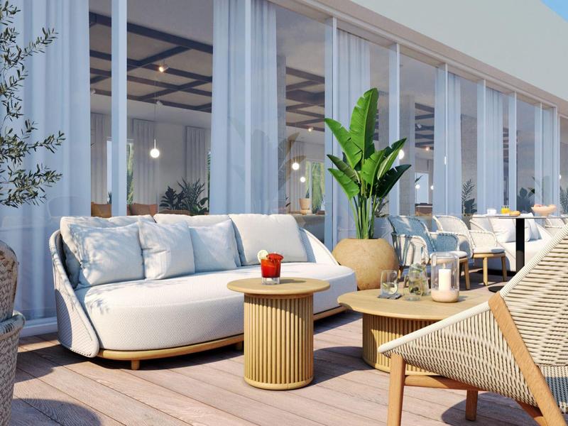 Modernes Terrassenmöbel mit Sofa, Stuhl und Pflanzen vor großen Glasfenstern eines Hotels.