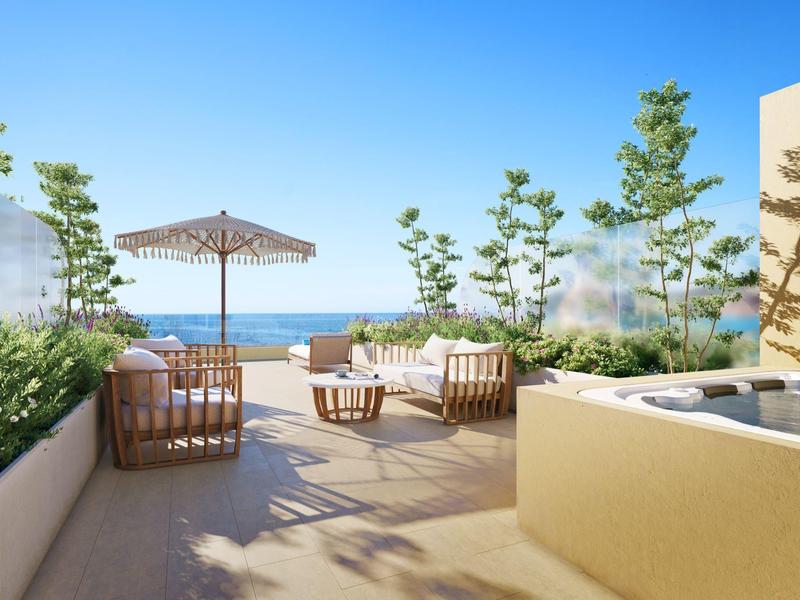 Terrasse mit Sitzbereich, Sonnenschirm und Blick auf das Meer an einem sonnigen Tag.