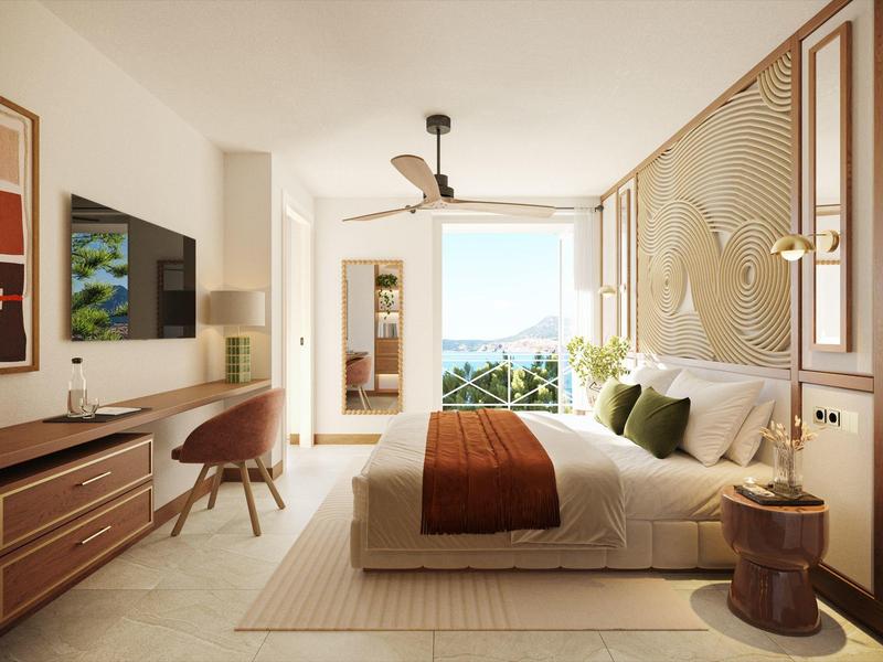 Helles Hotelzimmer mit Doppelbett, Schreibtisch, Fernseher und Balkon mit Meerblick.