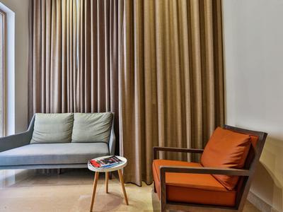 Modern living room area with grey sofa, orange armchair, and small round table in front of heavy curtains.