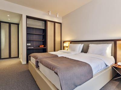 Modernes Hotelzimmer mit zwei Einzelbetten, Nachttischlampen und offenem Schrank.