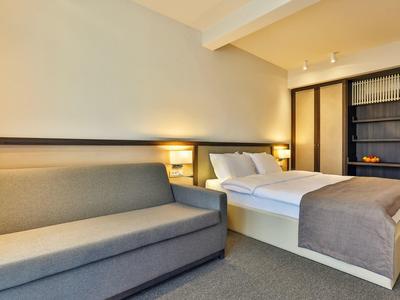 Modernes Hotelzimmer mit einem Bett, grauem Sofa und einem eingebauten Regal.