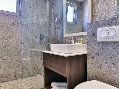 Modernes Badezimmer mit grauen Fliesen, WC, Waschbecken und großem Spiegel.