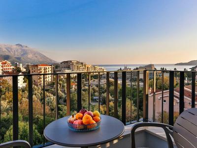 Balkon mit Tisch und Obstschale, Blick auf Häuser und Berge bei klarem Himmel.