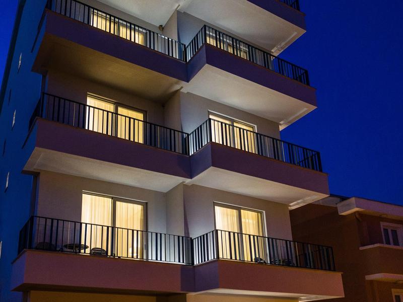 Mehrstöckiges Hotelgebäude mit beleuchteten Balkonen und Fenstern bei Nacht.