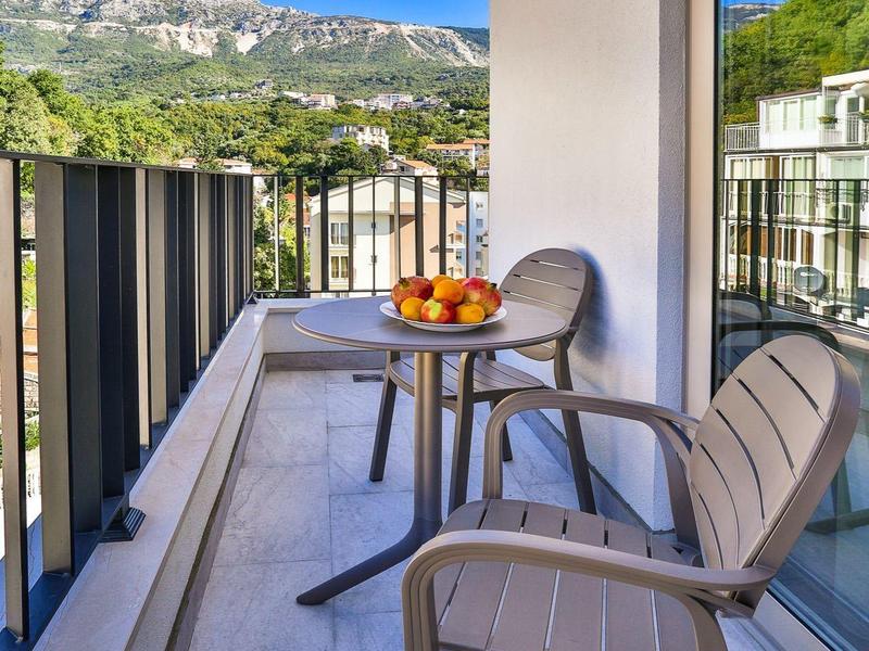 Balkon mit zwei Stühlen und Tisch mit Obstschale vor Bergkulisse.