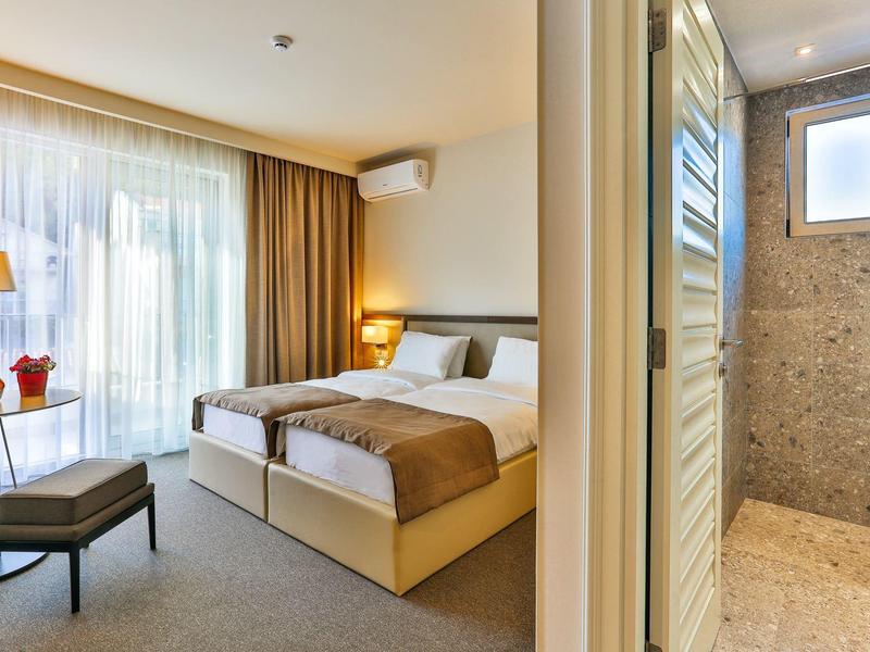 Modernes Hotelzimmer mit Doppelbett, Tisch, Stuhl und angrenzendem Badezimmer mit Dusche.