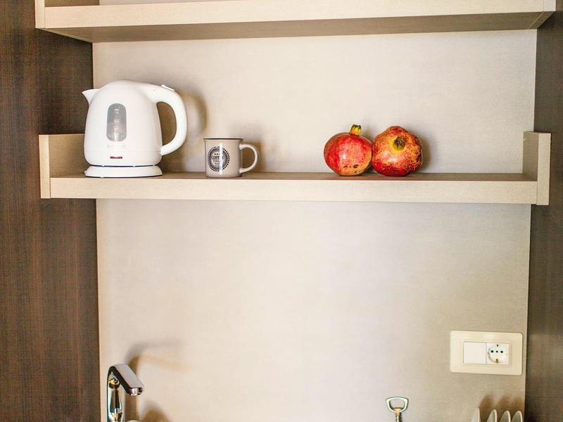 Kleine Küchenecke mit Spüle, Wasserkocher, Tassen, Äpfeln und Besteckablage.