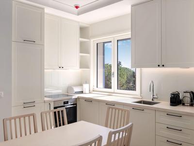 Moderne helle Küche mit weißen Schränken, Esstisch und Stühlen neben einem Fenster mit Aussicht.