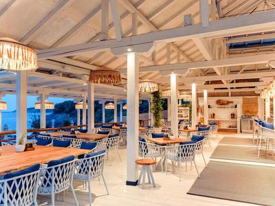 Helles und stilvolles Restaurant mit Holzdecke, blau-weißen Stühlen und Blick auf das Meer.