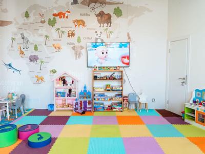Bunte Kinderspielecke mit Weltkartenwand, Spielzeug und Sitzkissen in einem hellen Raum.