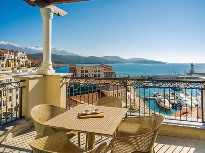 Balkon mit Sitzbereich und Blick auf Hafen und Berge bei klarem Himmel