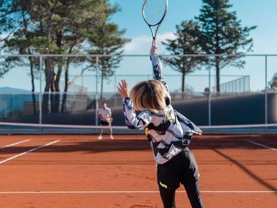 Person spielt Tennis auf einem roten Sandplatz an einem sonnigen Tag.