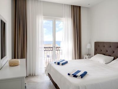 Helles Hotelzimmer mit großem Bett, Balkon mit Aussicht und modernen Vorhängen.