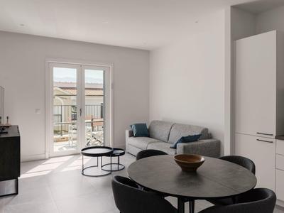 Moderner Wohnraum mit grauem Sofa, runden Tischen und Zugang zu einem Balkon.