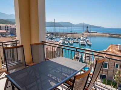 Balkon mit Glas- und Metalltisch und Stühlen mit Blick auf einen Hafen mit Segelbooten und Meer.