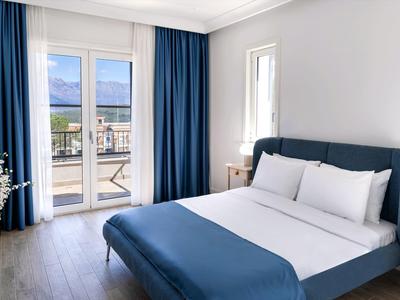 Modernes Gästezimmer mit großem Bett, blauen Vorhängen und Zugang zu Balkon mit Blick auf Außenbereich.