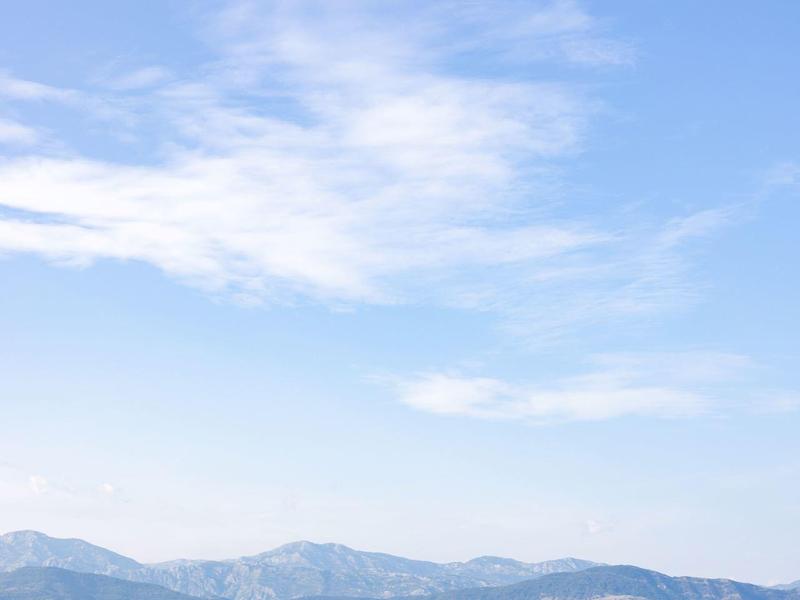 Grüne Wiese mit Zaun im Vordergrund, dahinter Berge unter blauem Himmel mit wenigen Wolken.