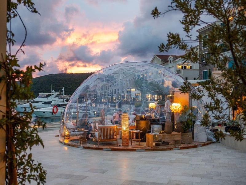 Glaskuppel auf Terrasse mit Sitzplatz und Meerblick bei Sonnenuntergang.