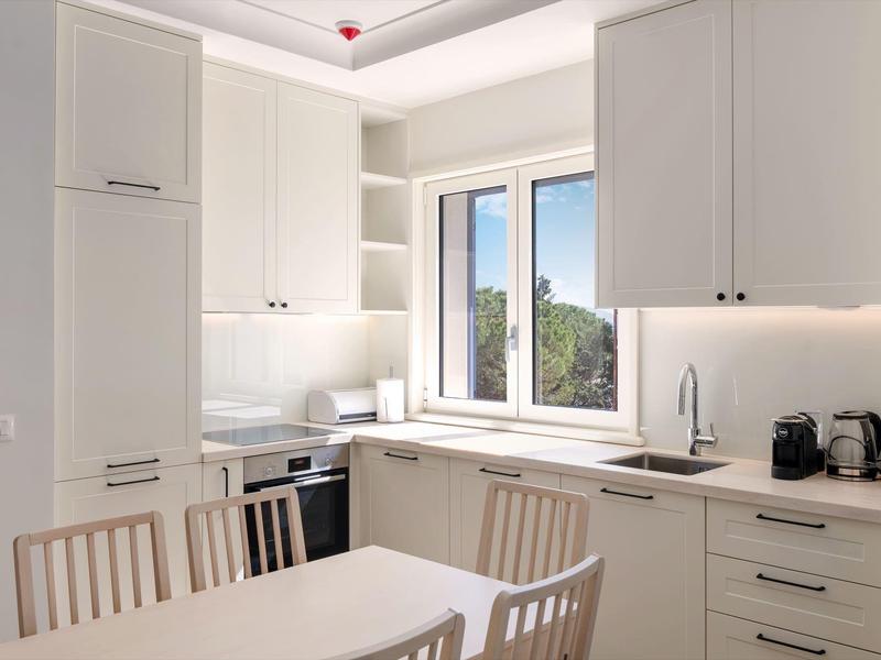 Moderne helle Küche mit weißen Schränken, Esstisch und Stühlen neben einem Fenster mit Aussicht.