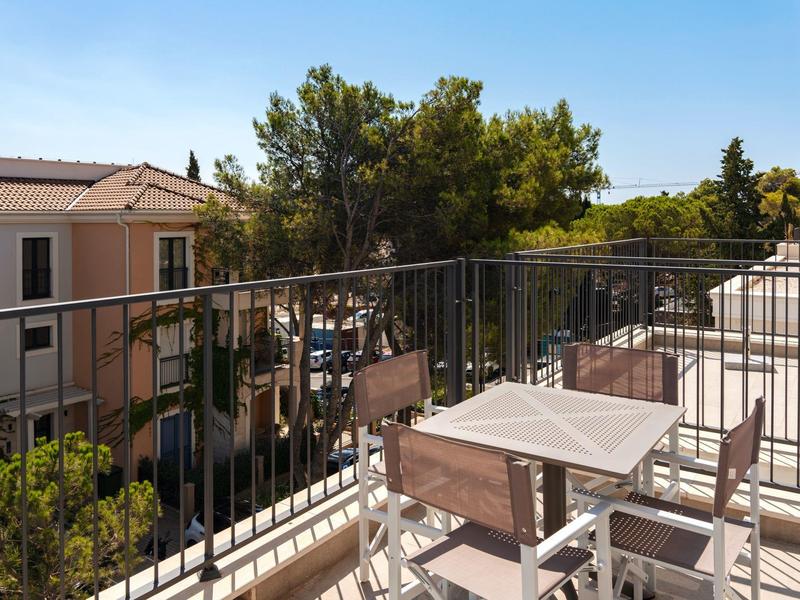 Balkon mit Metallgeländer, Tisch und Stühlen mit Blick auf Bäume und Gebäude.