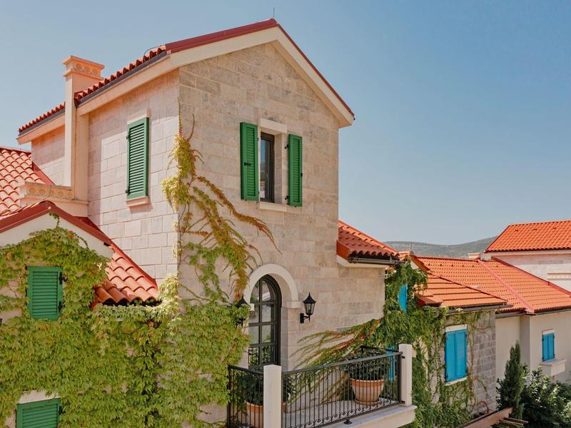Steinhaus mit roten Dachziegeln und grünen Fensterläden in sonniger Landschaft.