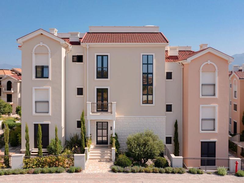 Modernes dreistöckiges Hotelgebäude mit hellen Wänden und grüner Bepflanzung im Vordergrund.