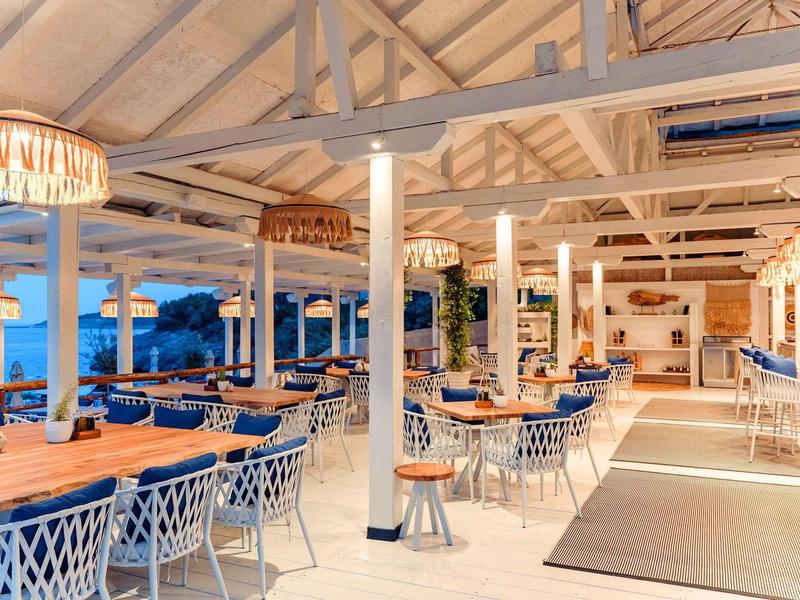 Helles und stilvolles Restaurant mit Holzdecke, blau-weißen Stühlen und Blick auf das Meer.