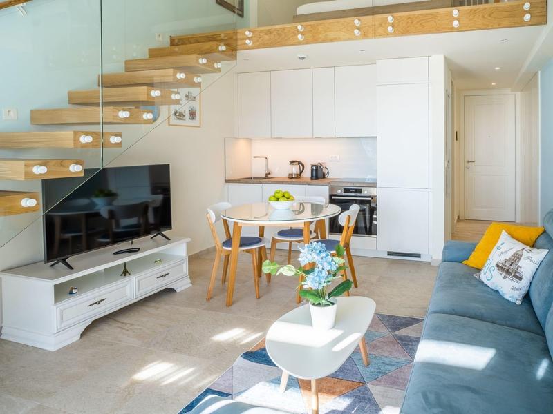 Modernes Wohnzimmer mit schwebender Holztreppe, Küchenzeile und gemütlichem Sofa.