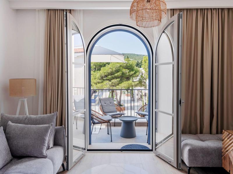 Blick durch offene französische Türen zu Balkon mit Sitzbereich und mediterraner Landschaft