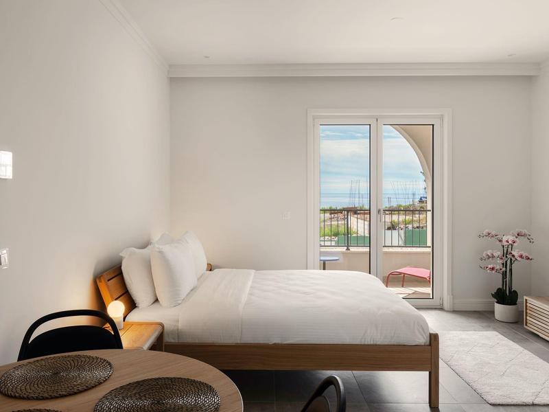 Helles Schlafzimmer mit Doppelbett, Balkontür mit Blick auf Wasser und Terrasse.