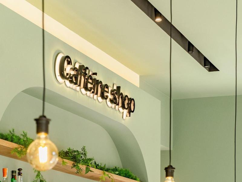 Moderne Cafétheke mit Tresen, Glühbirnen und Regalen voller Getränke und Dekoration.