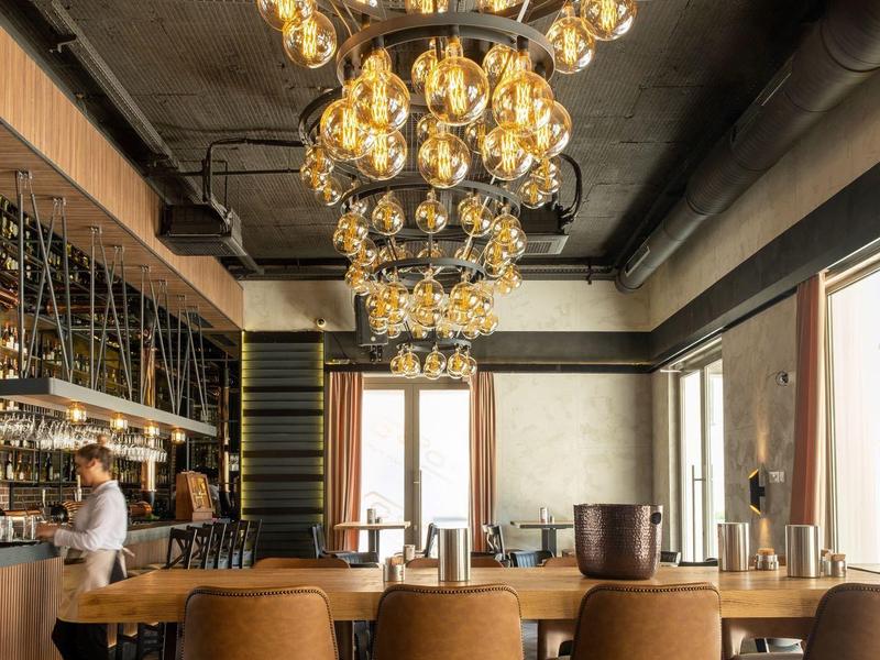 Elegante Bar mit modernen Hockern und großen Kronleuchtern in warmem Licht.